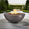 The Outdoor Plus 48" Sedona Wide Ledge Concrete Gas Fire Pit in brown, showcased in a sophisticated outdoor seating area. The fire pit features a modern bowl shape and a wide ledge, providing a functional yet stylish focal point for gatherings. The earthy brown finish complements the surrounding natural elements, making it perfect for patios, decks, and contemporary outdoor settings. This fire pit is designed to bring warmth and visual appeal to your outdoor space