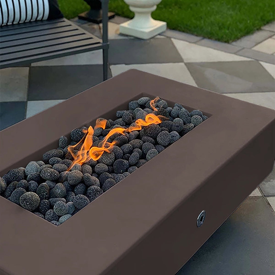 The Outdoor Plus 60-inch Del Mar Concrete Gas Fire Pit in rich chestnut color, a stunning outdoor centerpiece with glowing flames and dark lava rocks. This rectangular gas fire pit enhances outdoor spaces with its stylish design and ambient warmth.
