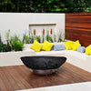 Lifestyle image of The Outdoor Plus round bowl fire pit cover placed over a decorative fire bowl in a modern patio setting, demonstrating its sleek design and superior weather protection. The cover's black fabric blends seamlessly with the outdoor décor while protecting the bowl from harsh weather elements. Perfect for safeguarding fire pits in residential or commercial settings.