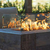 Lifestyle image of The Outdoor Plus 20"x20" Square Tempered Glass Wind Guard installed on a fire pit, showcasing tempered glass panels with polished edges. Protects flames from wind while maintaining visibility and elegance. Perfect for modern outdoor spaces and fire pits, ensuring safety and flame stability. Polished stainless steel brackets enhance the design.
